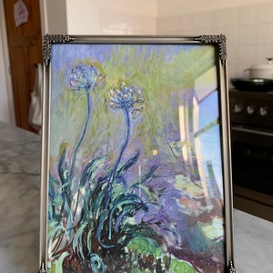 以下が含まれることがあります： 紫と緑の背景に青い花と緑の葉が描かれた絵画の額装されたプリントです。