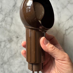 May include: A brown, vintage light fitting with a rounded top and a cylindrical base. The fitting has a dark interior and a visible lightbulb. The base has vertical ridges and metal prongs.