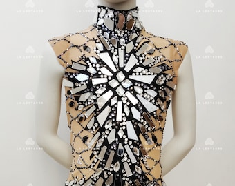 May include: A black leotard with a high neckline and a large, mirrored design on the front. The design is made up of many small, silver-colored pieces that are arranged in a geometric pattern. The leotard is made of a sheer fabric and has a nude lining.