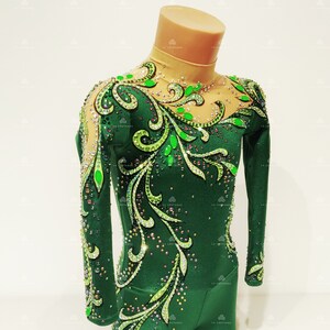 Pode incluir: Um maiô verde com mangas compridas e decote alto. O maiô é decorado com um design floral e strass.