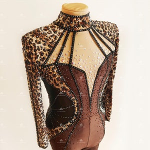 May include: A brown and black long-sleeved leotard with a leopard print design. The leotard has a high neckline and a mesh panel in the front that is decorated with rhinestones.