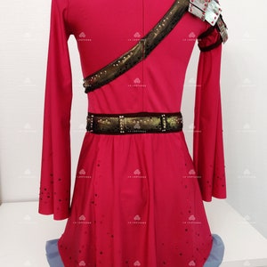 May include: A red figure skating dress with long sleeves and a gold and black belt. The dress is decorated with rhinestones and has a silver shoulder piece.