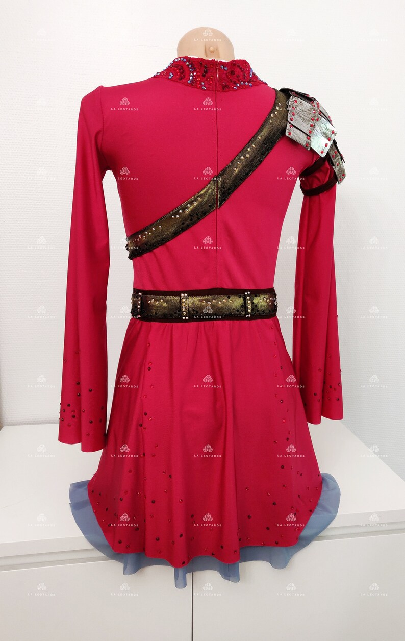 May include: A red figure skating dress with long sleeves and a gold and black belt. The dress is decorated with rhinestones and has a silver shoulder piece.