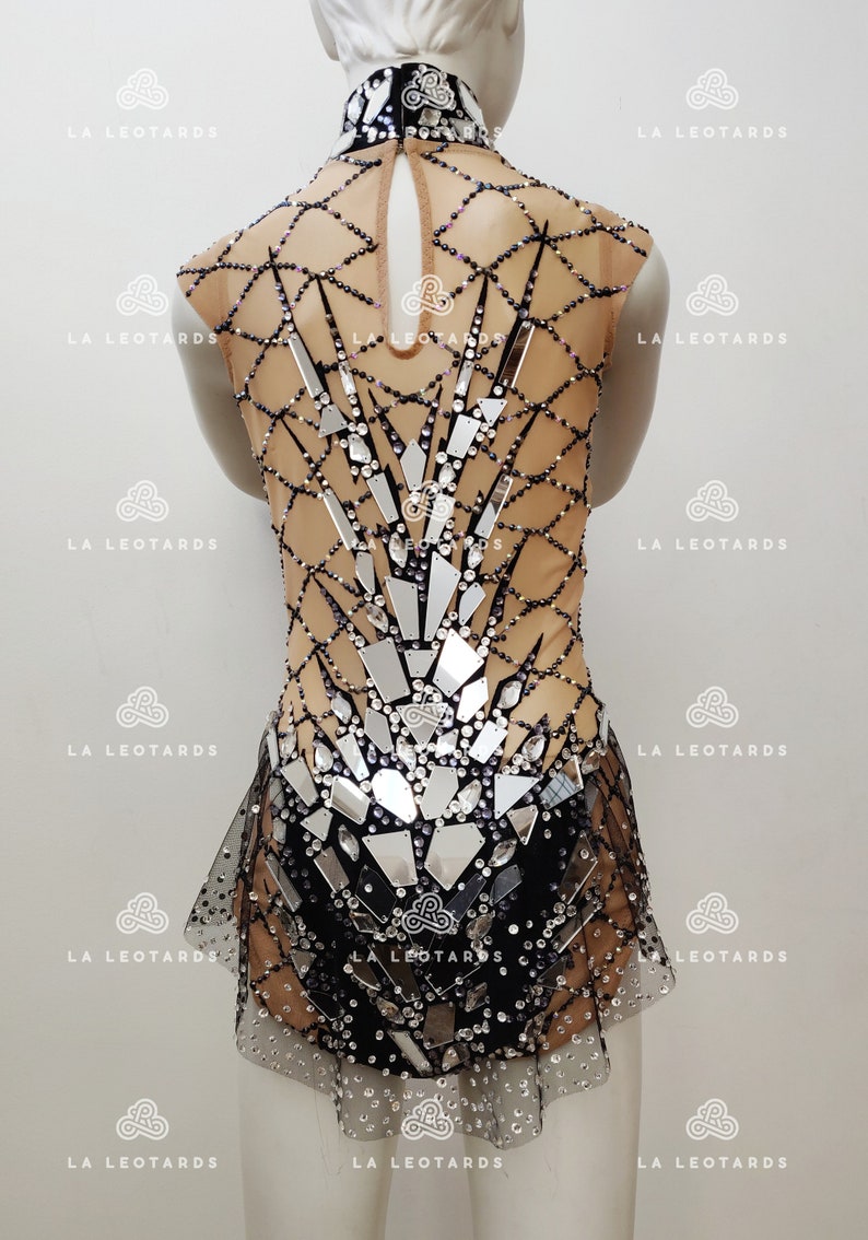 May include: A black and silver leotard with a mesh design and rhinestones. The leotard has a high neckline and a skirt.