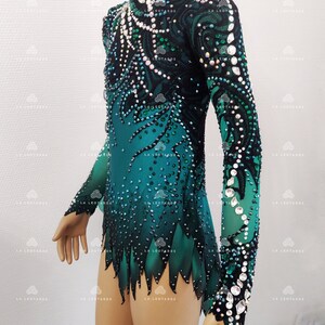 May include: A teal and black leotard with long sleeves, decorated with rhinestones and sequins. The high-neck leotard has a gradient design, changing from teal to black, and is embellished with detailed patterns. The sleeves are sheer, and the garment is designed for gymnastics or dance.