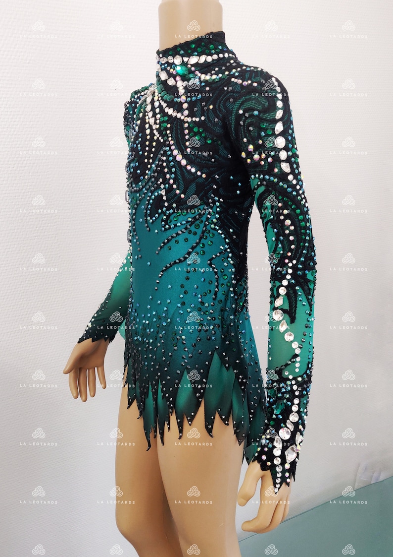 May include: A teal and black leotard with long sleeves, decorated with rhinestones and sequins. The high-neck leotard has a gradient design, changing from teal to black, and is embellished with detailed patterns. The sleeves are sheer, and the garment is designed for gymnastics or dance.