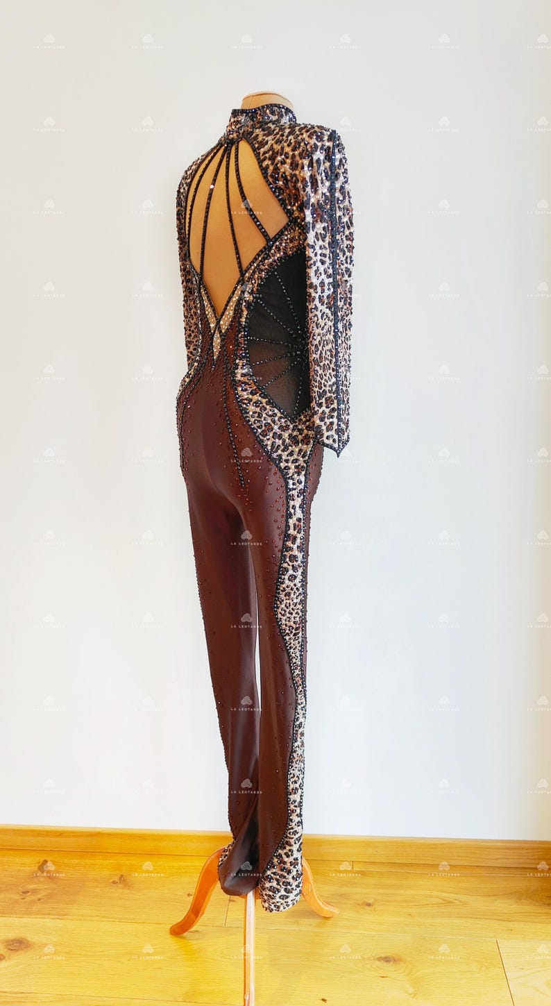 May include: A brown and black leopard print dance costume with a low back and rhinestones. The costume has long sleeves and a fitted silhouette.