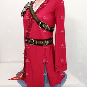 May include: A red figure skating dress with long sleeves, a white lace collar, and a brown belt with a buckle. The dress is decorated with rhinestones and has a gold and black trim. The dress has a short skirt with a blue tulle underskirt.