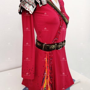 May include: A red, long-sleeved dress with a silver and black shoulder piece, a brown belt with rhinestones, and a colorful feather design on the skirt.