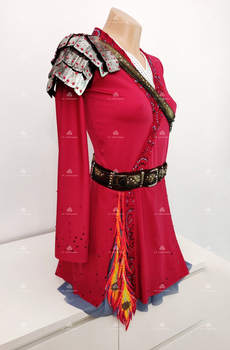 May include: A red, long-sleeved dress with a silver and black shoulder piece, a brown belt with rhinestones, and a colorful feather design on the skirt.