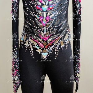 May include: Black leotard with long sleeves and a pink and silver rhinestone design. The leotard has a mesh panel in the front and a black fabric panel in the back. The leotard is decorated with rhinestones and sequins.