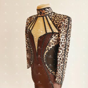 May include: A brown and black bodysuit with a leopard print design. The bodysuit has a high neckline and long sleeves. The bodice is embellished with rhinestones and has a sheer panel in the front.