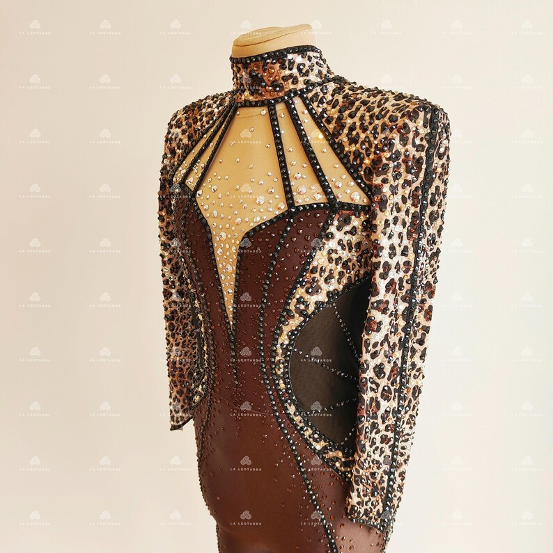 May include: A brown and black bodysuit with a leopard print design. The bodysuit has a high neckline and long sleeves. The bodice is embellished with rhinestones and has a sheer panel in the front.