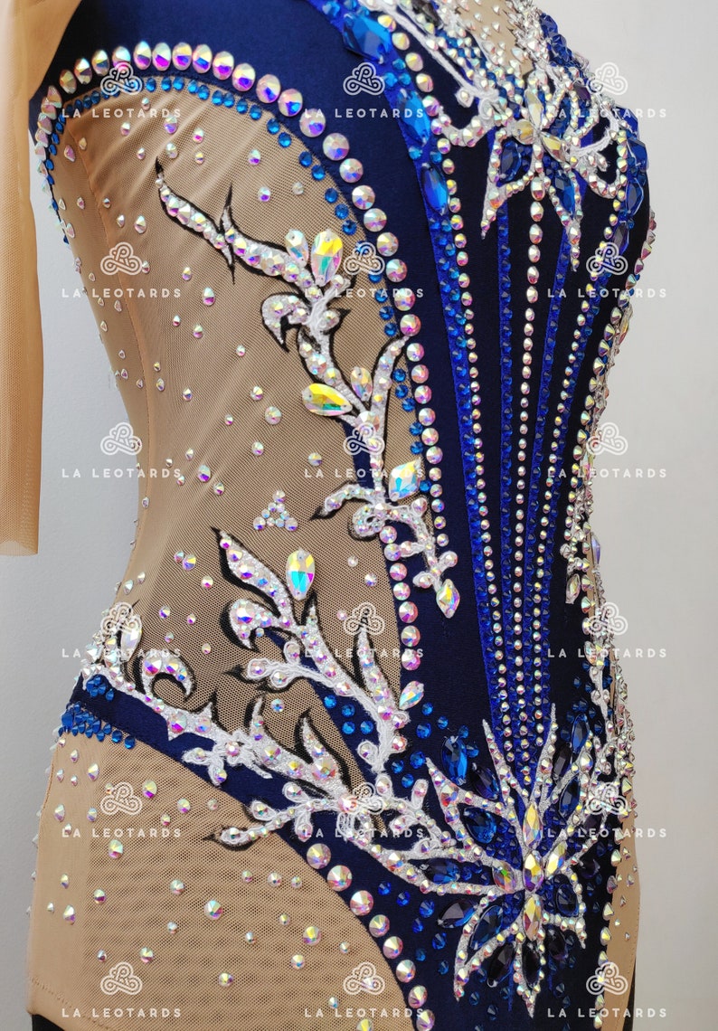 Pu&ograve; includere: Un body blu e bianco con un design floreale e strass. Il body &egrave; realizzato in un tessuto trasparente con una fodera color carne. Il body ha una scollatura rotonda e una schiena che &egrave; tagliata bassa. Il body &egrave; decorato con strass di varie dimensioni e colori. Il body &egrave; perfetto per la ginnastica, la danza o il pattinaggio artistico.