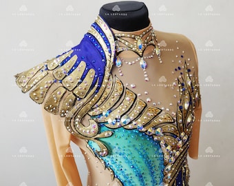May include: A nude-colored leotard with a blue and gold design. The leotard is decorated with rhinestones and has a high neckline. The design features a large wing-like shape on the shoulder and a smaller wing-like shape on the chest.