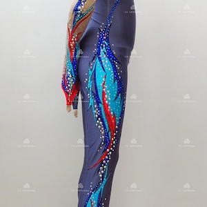 Op de afbeelding: Een grijze maillot met lange mouwen en een kleurrijk ontwerp met blauwe, rode en turquoise accenten. De maillot is versierd met strass en heeft een aansluitende pasvorm.