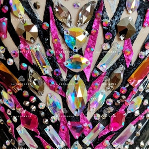 May include: Close-up of a black leotard with pink and black ribbon accents and iridescent rhinestones.