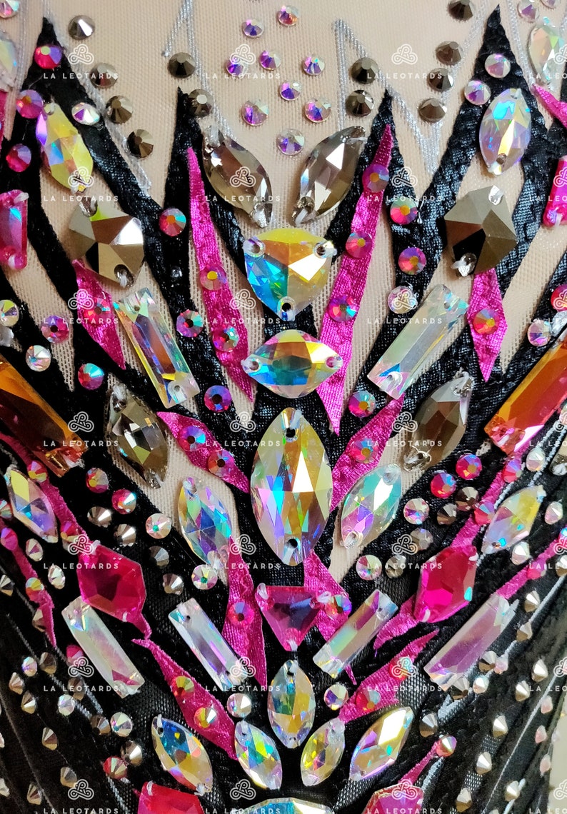 May include: Close-up of a black leotard with pink and black ribbon accents and iridescent rhinestones.
