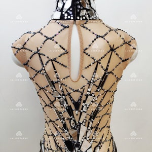 May include: A black and nude leotard with a high neckline and a geometric design featuring mirrored pieces and rhinestones.