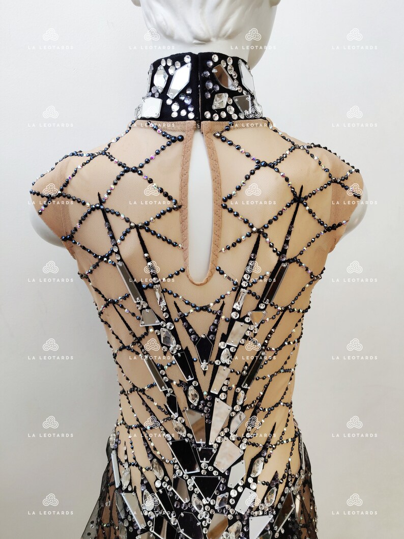 May include: A black and nude leotard with a high neckline and a geometric design featuring mirrored pieces and rhinestones.