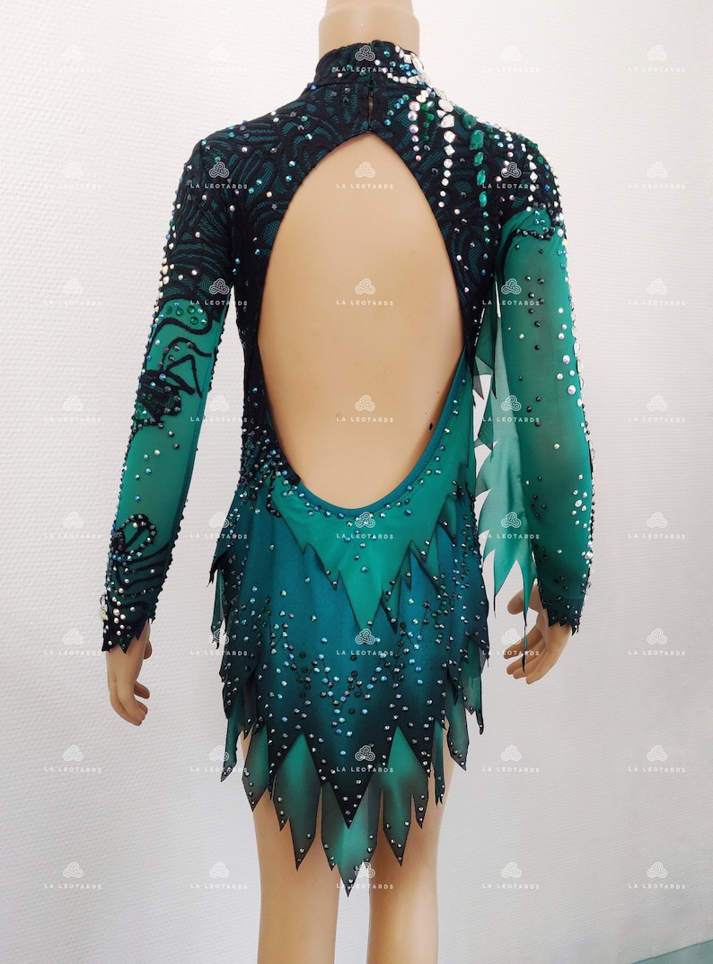 May include: A teal and black leotard with long sleeves and an open back. The leotard is embellished with sequins and features a high neckline and a unique skirt design with pointed edges. The sleeves are sheer.