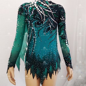 May include: A teal and black leotard with long sleeves, adorned with rhinestones. The leotard has a high neckline and a decorative pattern on the bodice and sleeves. The bottom hem has a jagged, leaf-like design. The brand "LA Leotards" is visible.