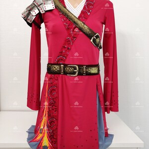 May include: A red and gray figure skating dress with a gold belt, a silver shoulder piece, and a colorful feather detail. The dress is decorated with rhinestones.
