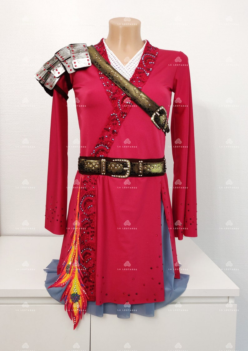 May include: A red and gray figure skating dress with a gold belt, a silver shoulder piece, and a colorful feather detail. The dress is decorated with rhinestones.