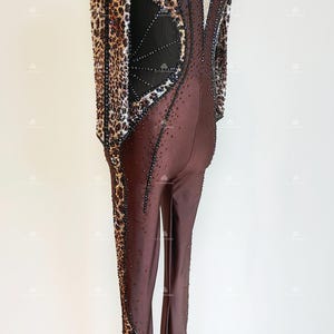 May include: A brown and black jumpsuit with a leopard print design. The jumpsuit has a high neck and long sleeves. The back of the jumpsuit features a mesh panel with a geometric design.