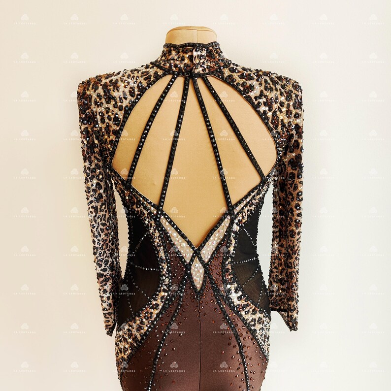 May include: A brown and black long-sleeved dance dress with a leopard print design. The dress has a low back with a geometric pattern of black straps and rhinestones.