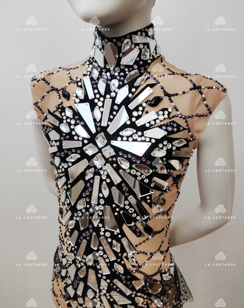 May include: A black leotard with a high neckline and short sleeves. The leotard is covered in rhinestones and mirrored pieces, creating a sparkling and eye-catching design.