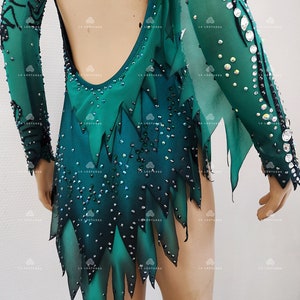 May include: A green and black leotard with long sleeves, adorned with rhinestones. The backless design showcases a gradient of green shades and a jagged, leaf-like hem. The sleeves are sheer, and the garment is designed for performance.