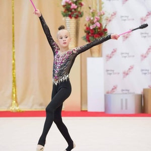 May include: A young girl in a black leotard with a sparkly design performs a rhythmic gymnastics routine with two pink and black clubs.