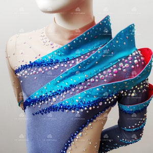 Op de afbeelding: Een grijs, blauw en turquoise turnpakje met een gelaagd ontwerp en strass steentjes. Het turnpakje heeft lange mouwen en een hoge halslijn.