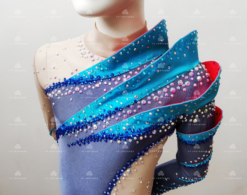 Op de afbeelding: Een grijs, blauw en turquoise turnpakje met een gelaagd ontwerp en strass steentjes. Het turnpakje heeft lange mouwen en een hoge halslijn.