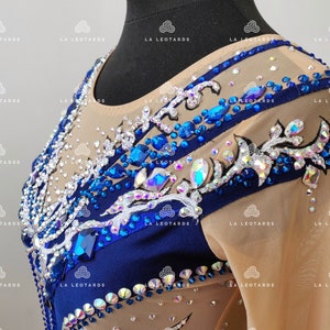Pu&ograve; includere: Un body blu e bianco con strass e un design floreale. Il body &egrave; realizzato in tessuto trasparente e ha maniche lunghe.