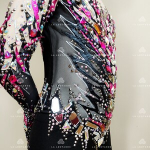 May include: Black leotard with long sleeves and a black and white zebra print design. The leotard is embellished with rhinestones and mirrored pieces in various shapes and sizes. The rhinestones are pink, clear, and iridescent.