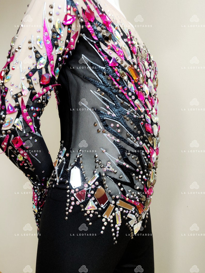 May include: Black leotard with long sleeves and a black and white zebra print design. The leotard is embellished with rhinestones and mirrored pieces in various shapes and sizes. The rhinestones are pink, clear, and iridescent.