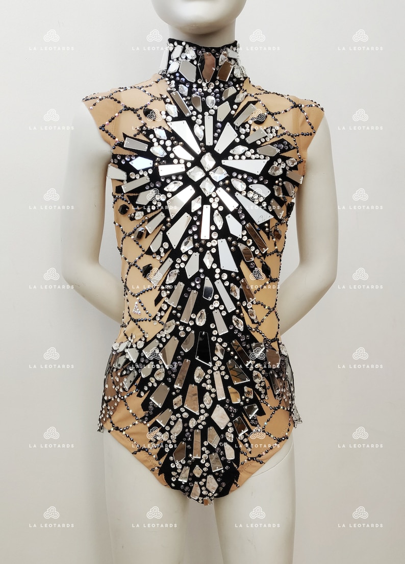 May include: A black leotard with a high neckline and a large, mirrored design on the front. The design is made up of many small, silver-colored pieces that are arranged in a geometric pattern. The leotard is made of a sheer fabric and has a nude lining.