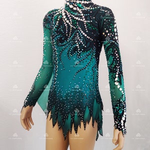 May include: A teal and black leotard with long sleeves, decorated with rhinestones. The design includes a high neckline and a decorative pattern flowing down the bodice. The sleeves are sheer, and the hem has a jagged edge. The brand name "LA LEOTARDS" is visible.