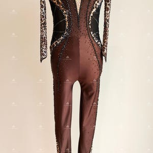 May include: A brown and black dance leotard with a leopard print design and rhinestones. The leotard has long sleeves and a high neckline.