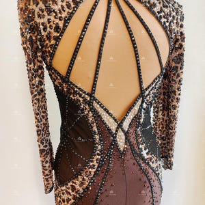 May include: A brown and black dance leotard with a leopard print design and rhinestones. The leotard has a high neckline and long sleeves. The back of the leotard has a large cutout with a geometric design.