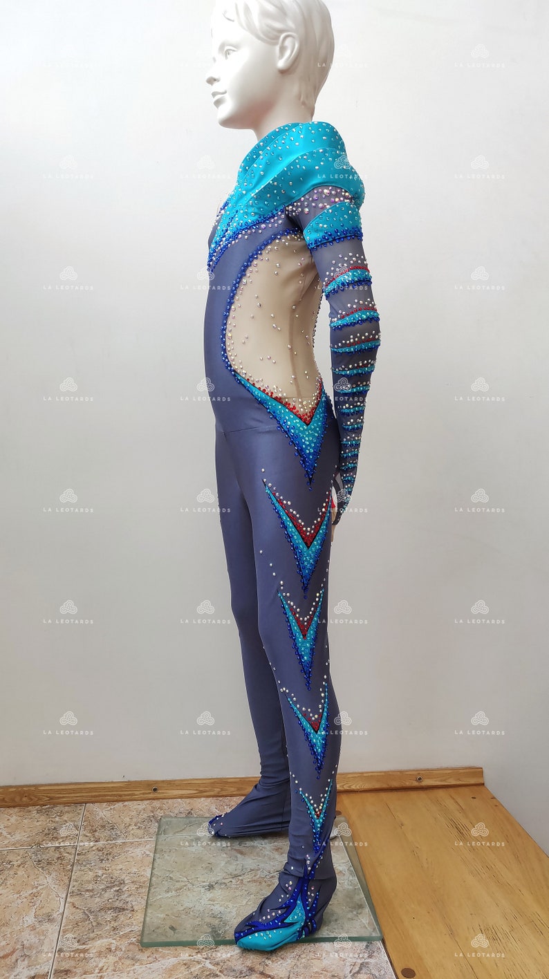 Op de afbeelding: Een grijs pakje met blauwe en turquoise accenten en strass. Het pakje heeft lange mouwen en een hoge hals. Het pakje is ontworpen voor kunstschaatsen.