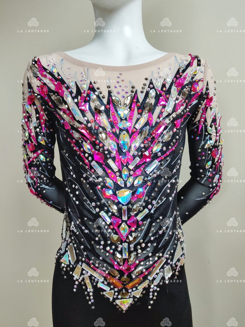 May include: Black leotard with long sleeves and a pink and silver rhinestone design. The leotard has a scoop neck and a fitted silhouette.