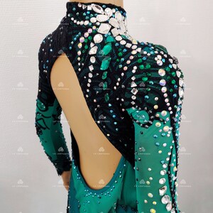 May include: A green and black leotard with long sleeves, adorned with rhinestones and crystals. The leotard has a high neck and an open back design. The sleeves have a gradient effect, changing from green to black. The garment is designed for dance or gymnastics.