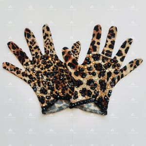 May include: A pair of brown and black leopard print gloves with rhinestones. The gloves are made of a stretchy fabric and have a fitted design.