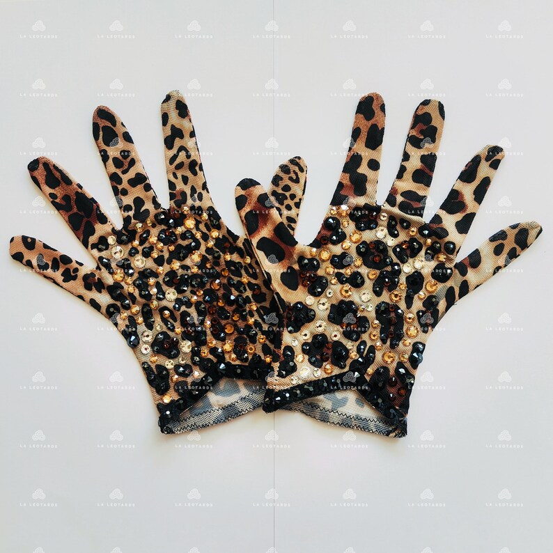 May include: A pair of brown and black leopard print gloves with rhinestones. The gloves are made of a stretchy fabric and have a fitted design.