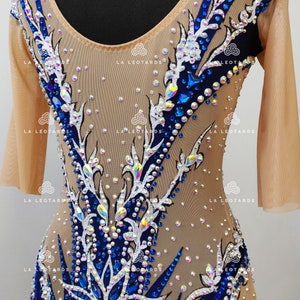 Pu&ograve; includere: Un body color carne con maniche lunghe e scollo rotondo. Il body &egrave; decorato con un motivo floreale in strass bianchi e blu. Il motivo presenta un grande fiore al centro del body.