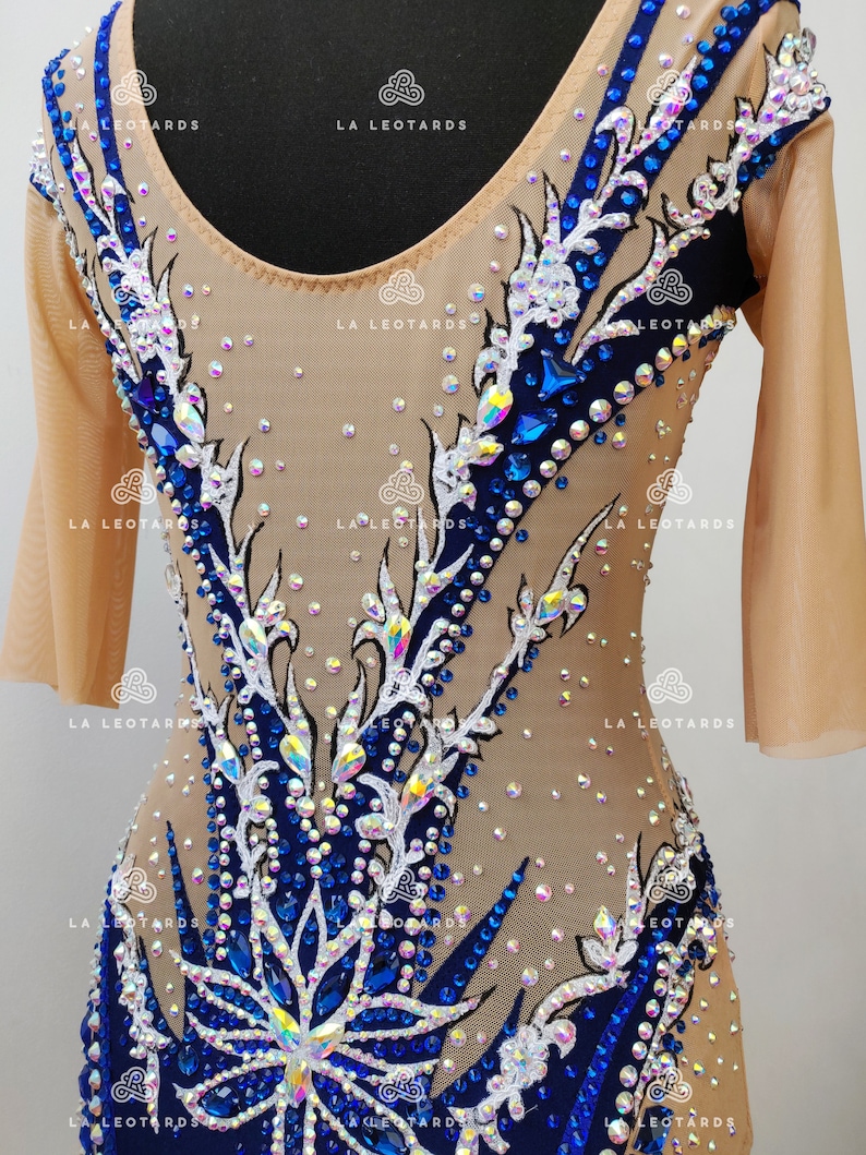 Pu&ograve; includere: Un body color carne con maniche lunghe e scollo rotondo. Il body &egrave; decorato con un motivo floreale in strass bianchi e blu. Il motivo presenta un grande fiore al centro del body.