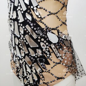 May include: A black leotard with a sheer mesh overlay and a design of silver and black rhinestones. The leotard has a scoop neck and a low back.